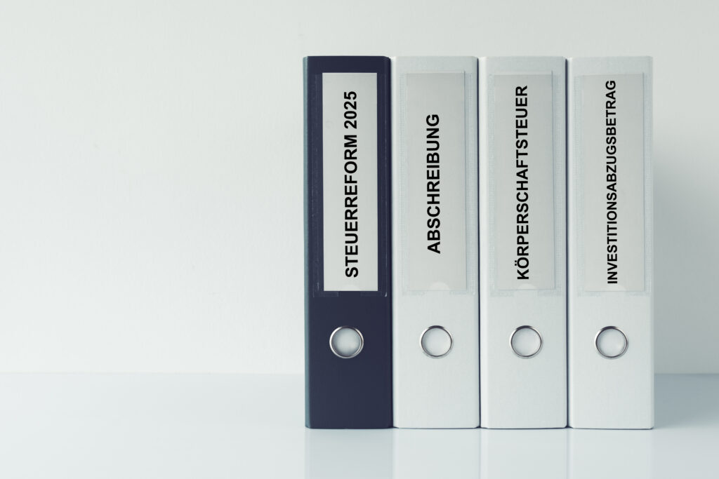 Reihe von Aktenordnern mit Aufschriften Steuerreform 2025, Abschreibung, Körperschaftsteuer und Investitionsabzugsbetrag – Symbol für Steuergesetze und Reformen.