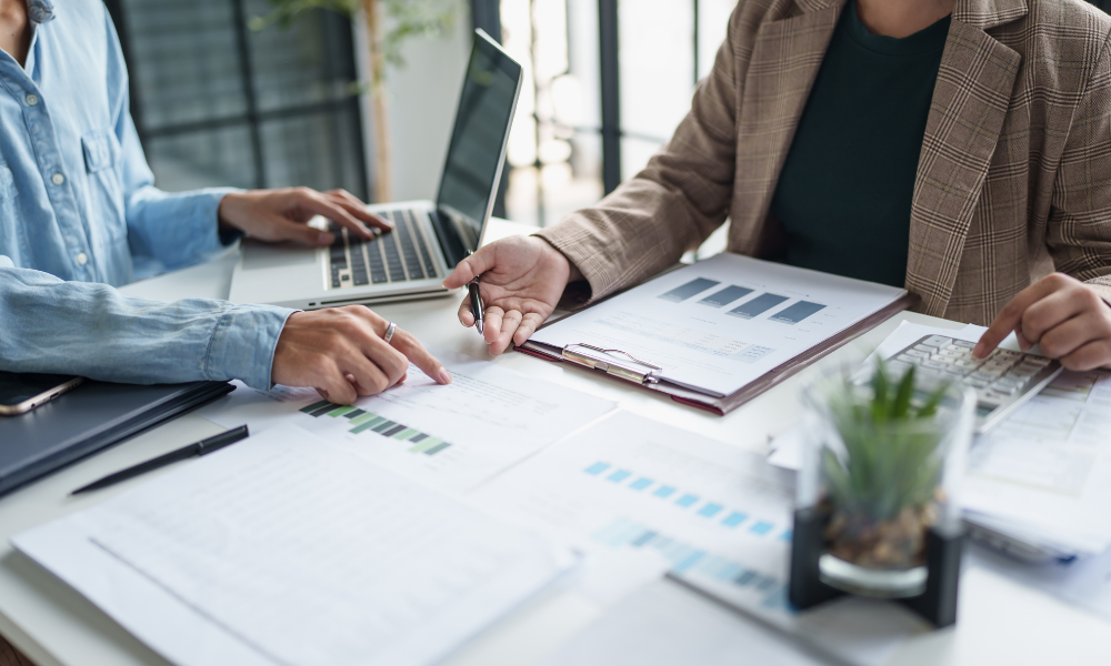 Zwei Personen besprechen Finanzunterlagen mit Diagrammen und Laptop, während ein Taschenrechner genutzt wird, als Symbol für steuerliche Planung und Investitionsentscheidungen beim Investitionsabzugsbetrag (IAB)