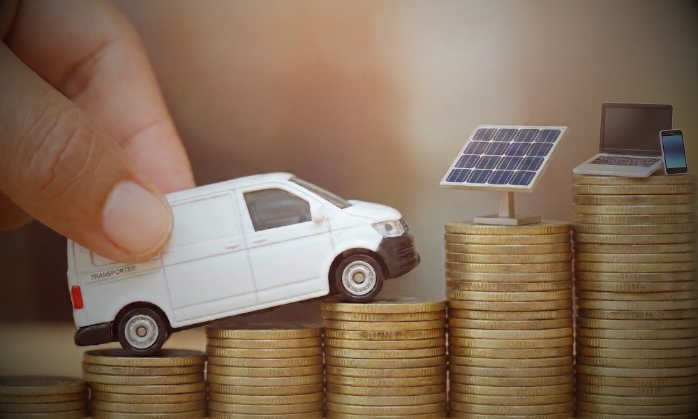 Hand schiebt ein Modell eines Transporters über gestapelte Münzen; daneben stehen weitere Münzstapel mit Solarmodul, Laptop und Smartphone als Symbole für geplante Investitionen und die Bildung eines Investitionsabzugsbetrags, passend zum Thema „Gewinn ist nicht gleich Liquidität“