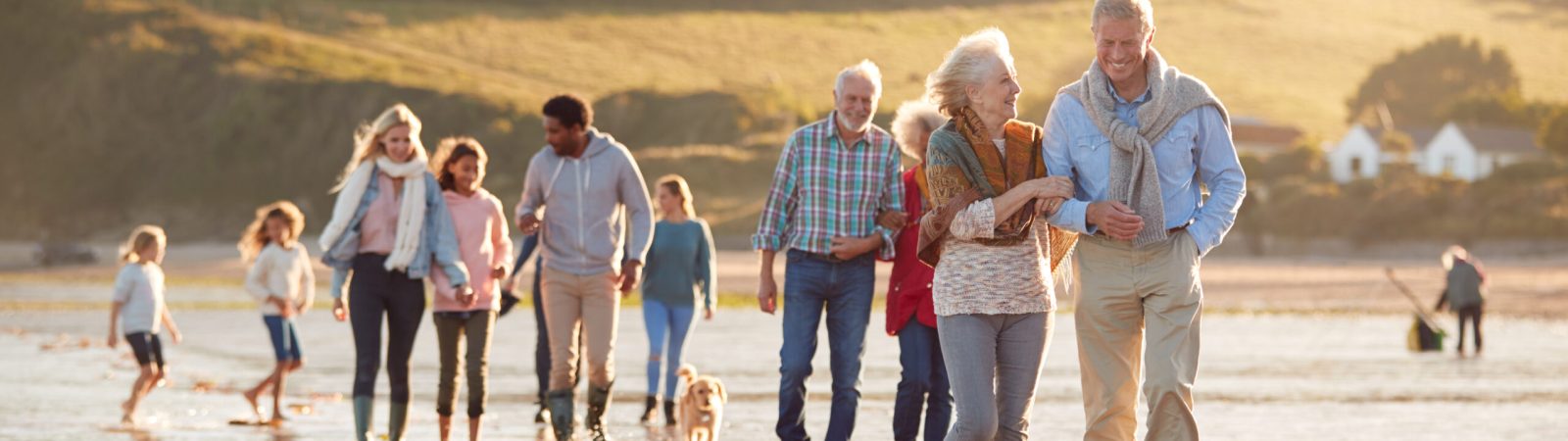 Mehrgenerationenfamilie spaziert am Strand mit Kindern und Hund – Symbol für Familie, Zusammenhalt und generationenübergreifende Sicherheit.