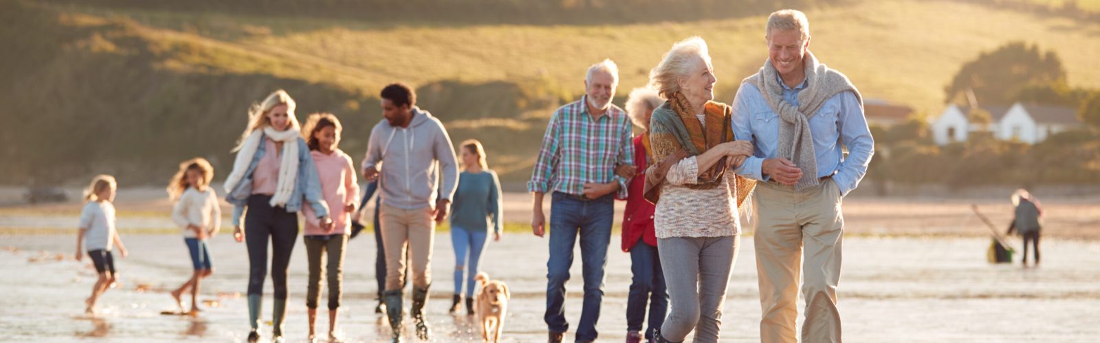 Mehrgenerationenfamilie spaziert am Strand mit Kindern und Hund – Symbol für Familie, Zusammenhalt und generationenübergreifende Sicherheit.