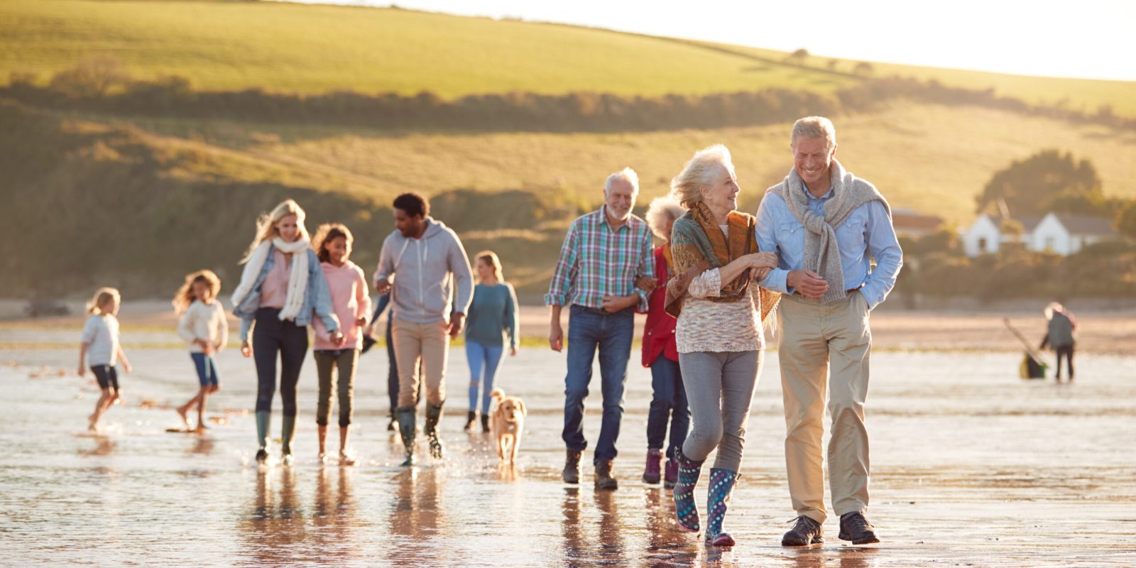 Mehrgenerationenfamilie spaziert am Strand mit Kindern und Hund – Symbol für Familie, Zusammenhalt und generationenübergreifende Sicherheit.