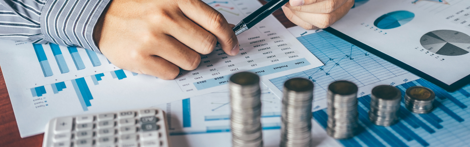 Person analysiert Finanzunterlagen mit Diagrammen und Tabellen zur Cashflow-Planung; daneben Taschenrechner und gestapelte Münzen