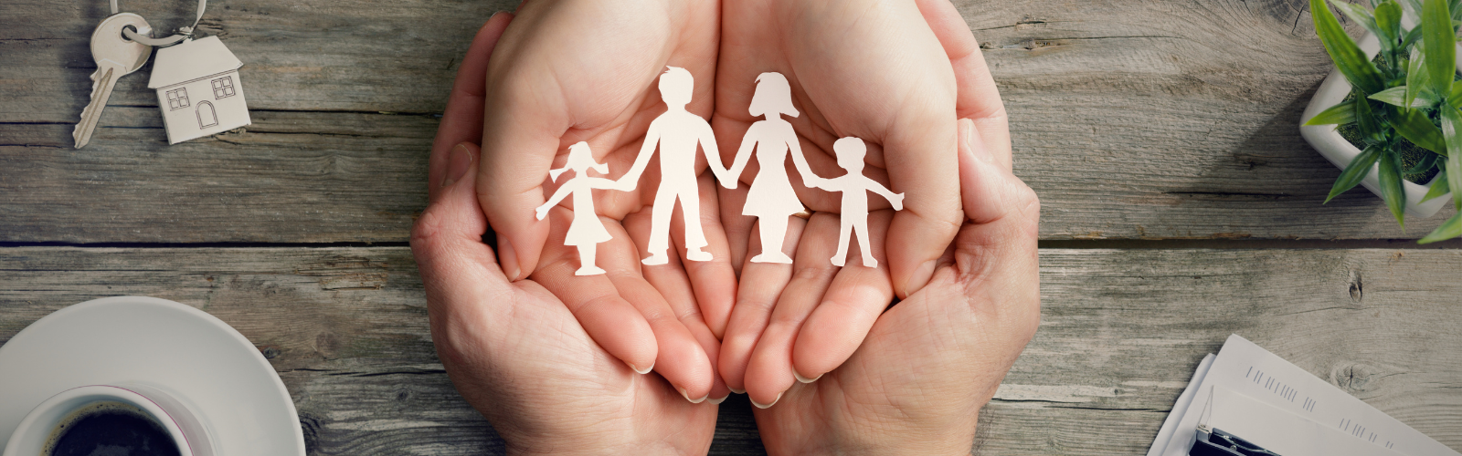 Zwei Hände halten eine Papierfigur einer Familie, daneben Schlüssel und Unterlagen, als Symbol für die Einbindung von Familienangehörigen im Unternehmen