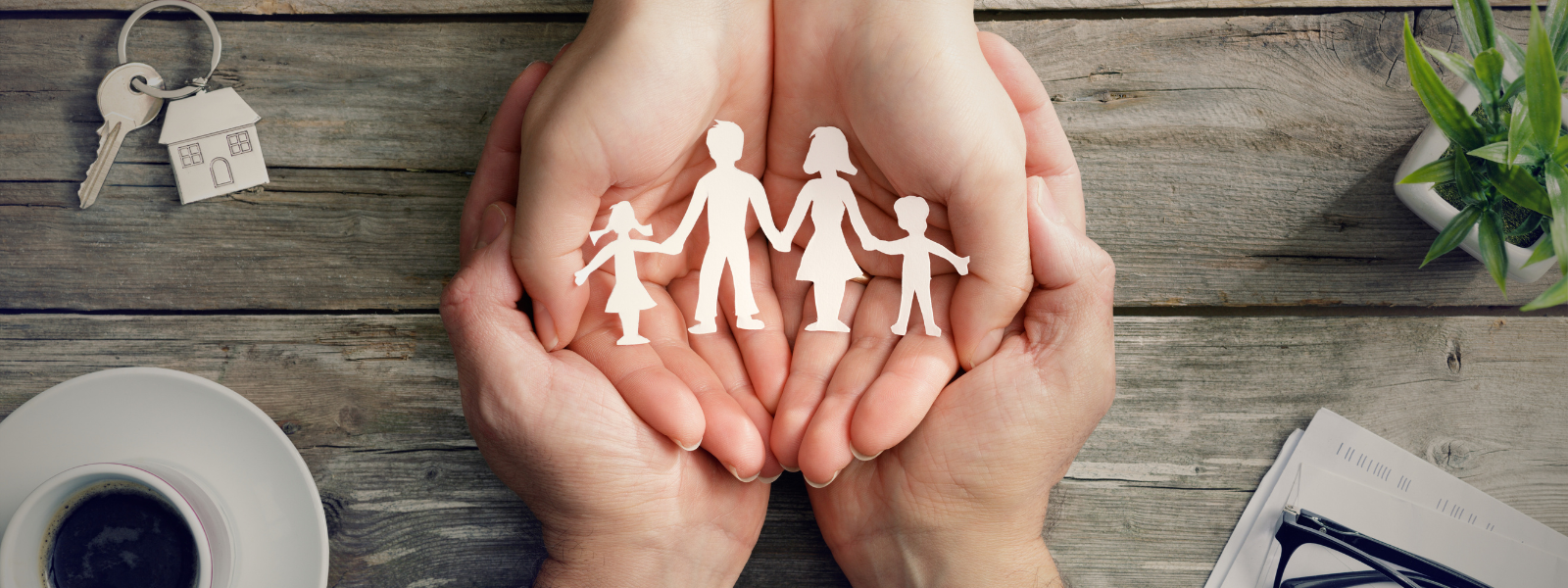 Zwei Hände halten eine Papierfigur einer Familie, daneben Schlüssel und Unterlagen, als Symbol für die Einbindung von Familienangehörigen im Unternehmen